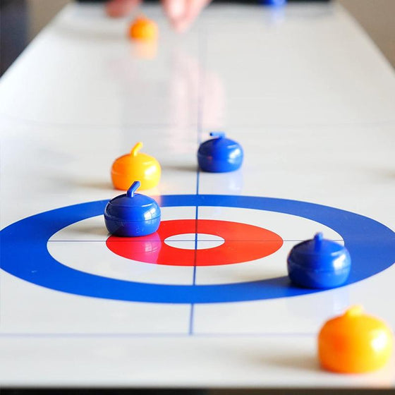 Spieler schiebt eine Curlingscheibe auf der Tischcurling-Matte. Familienspaß und Geschicklichkeitsförderung für Kinder.