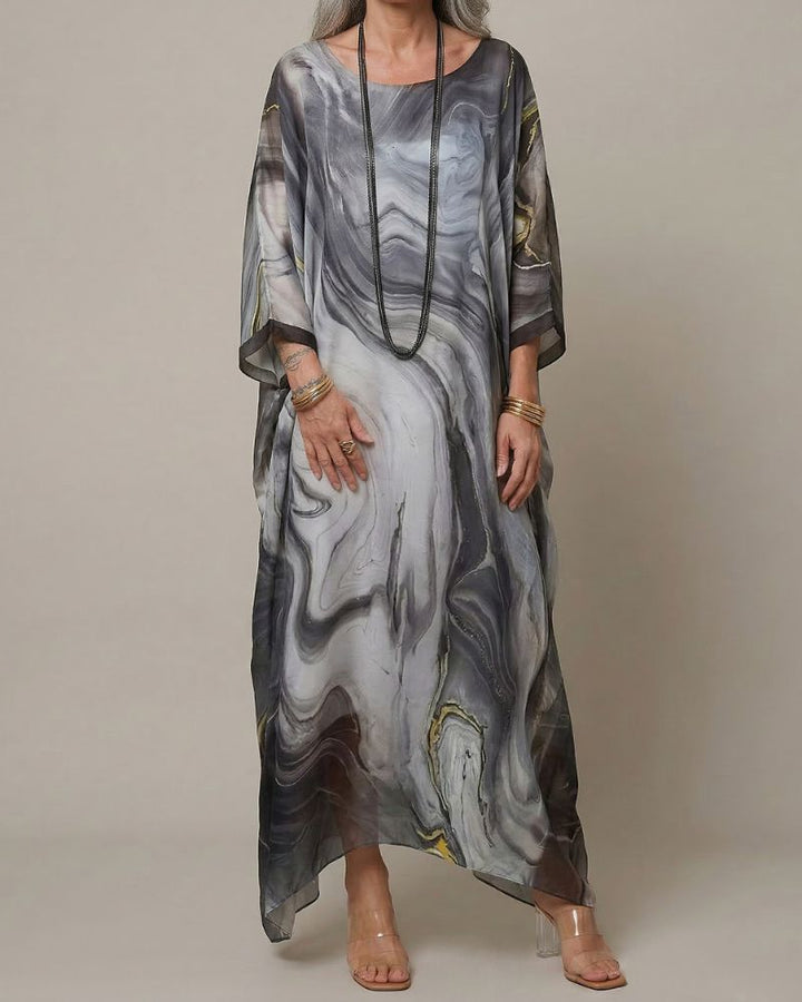 Dame trägt fließendes, asymmetrisches Maxikleid mit abstraktem Muster. Bequemes, langes Freizeit- und Sommerkleid.