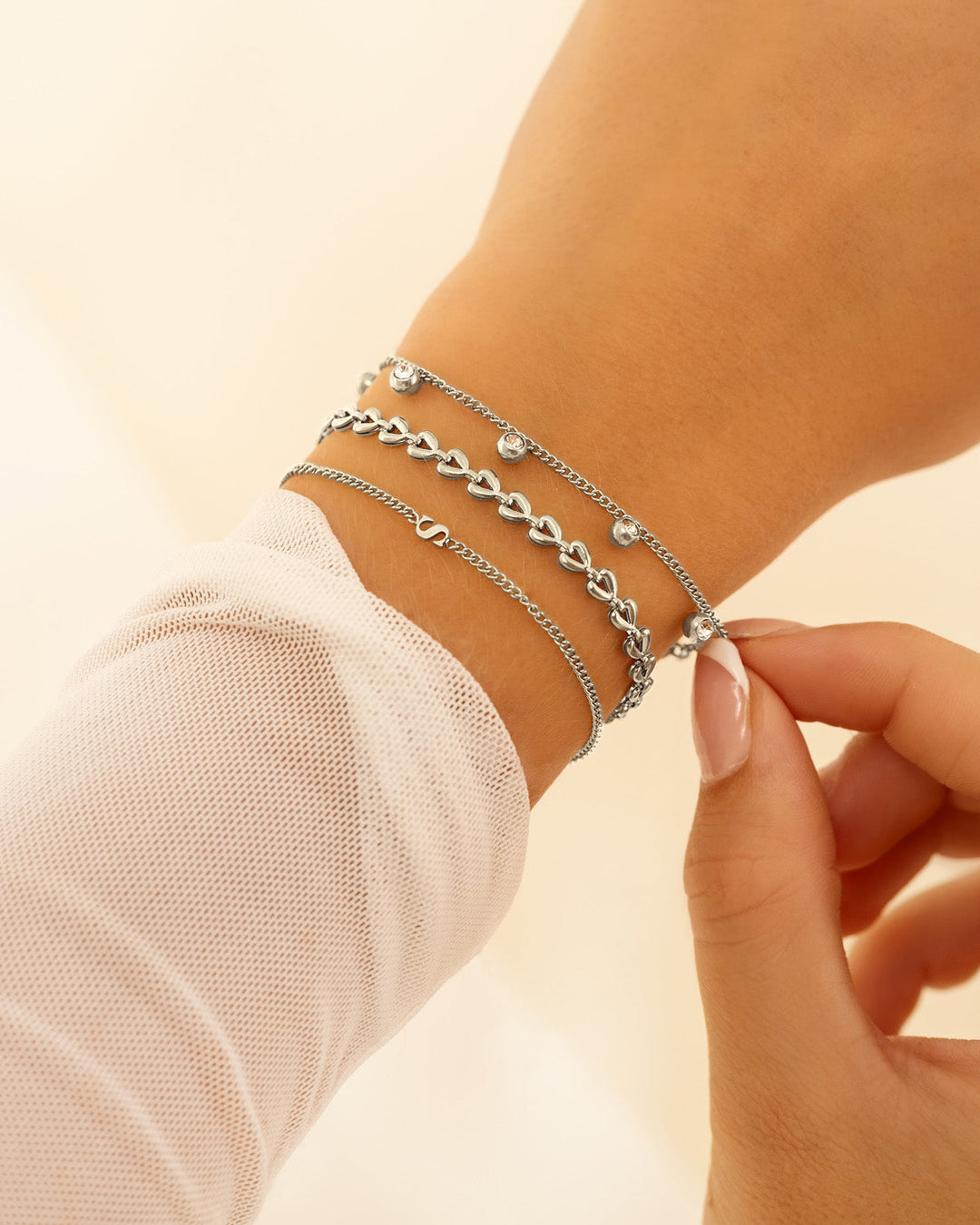 Damen-Initialarmband in Goldoptik, getragen mit weiteren Armbändern. Trendiger, personalisierter Look.