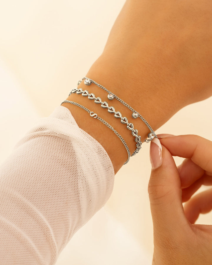 Damen-Initialarmband in Goldoptik, getragen mit weiteren Armbändern. Trendiger, personalisierter Look.
