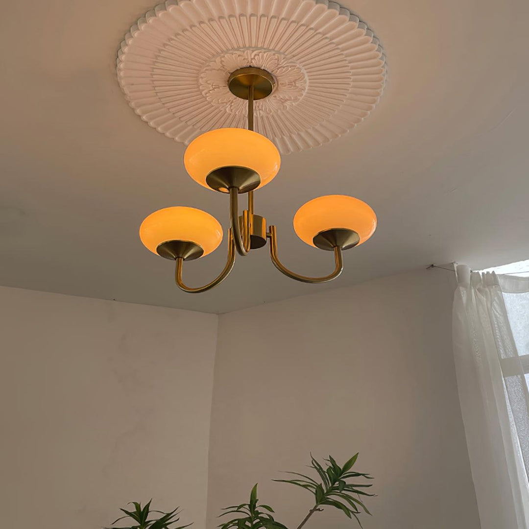 Goldener Kronleuchter mit zylindrischen Glas-Schirmen, leuchtet; helle und moderne Deckenleuchte.
