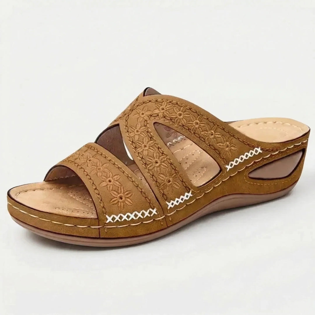 Frau trägt bequeme Damen Keilabsatz-Sandale mit Blumenmuster. Retro Slip-on Design für Alltag.