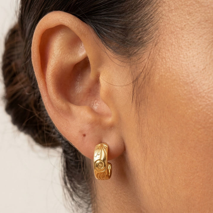Nahaufnahme: Goldene Edelstahl Creolen für Damen mit zartem Blumenmuster. Hypoallergen & wasserdicht, ideal für jedes Outfit.