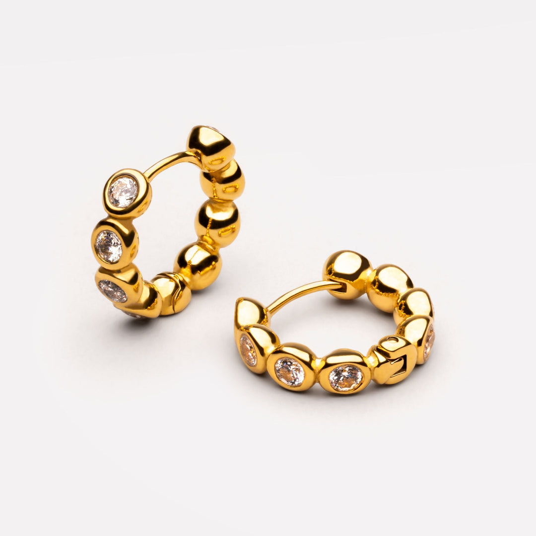 Goldfarbene Huggie Creolen für Damen mit funkelnden weißen Schmucksteinen, wasserfester Edelstahlschmuck.
