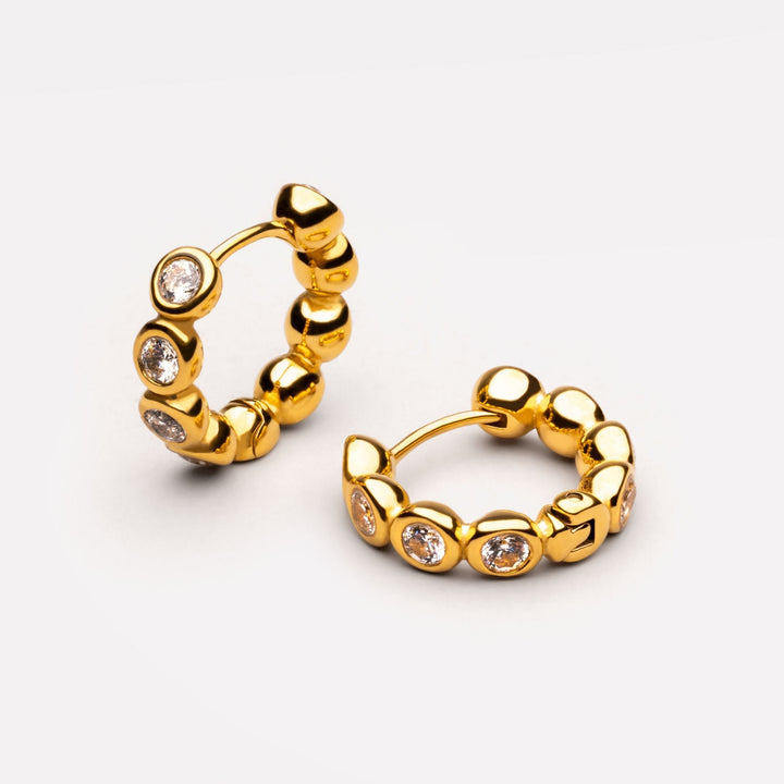 Goldfarbene Huggie Creolen für Damen mit funkelnden weißen Schmucksteinen, wasserfester Edelstahlschmuck.