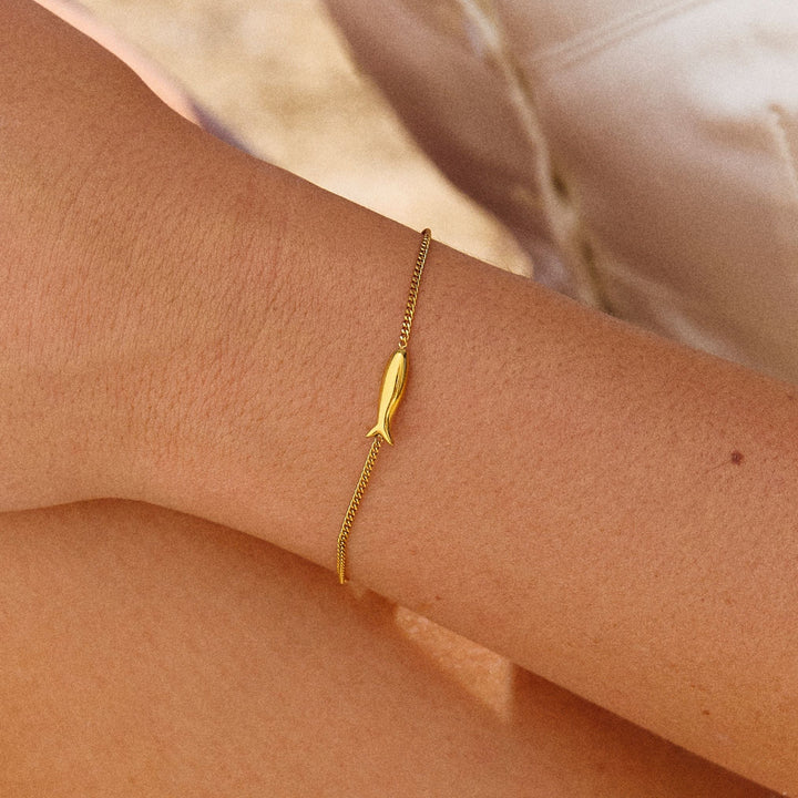 Elegantes Gold Damen Armband mit glänzendem Fischanhänger, wasserfest & verstellbar, aus Edelstahl.