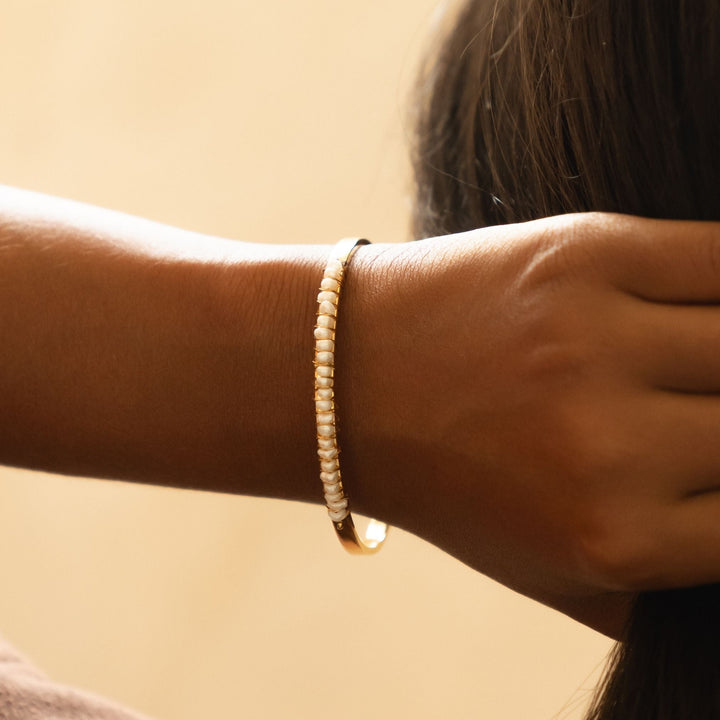 Nahaufnahme eines goldenen Damen Armreifs mit schimmernden Süßwasserperlen; wasserfest & für sensible Haut.