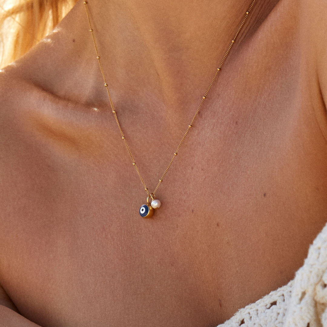 Trendige Kombi: Goldene Nazar Auge Halskette mit Süßwasserperle, gestylt mit weiteren Ketten.