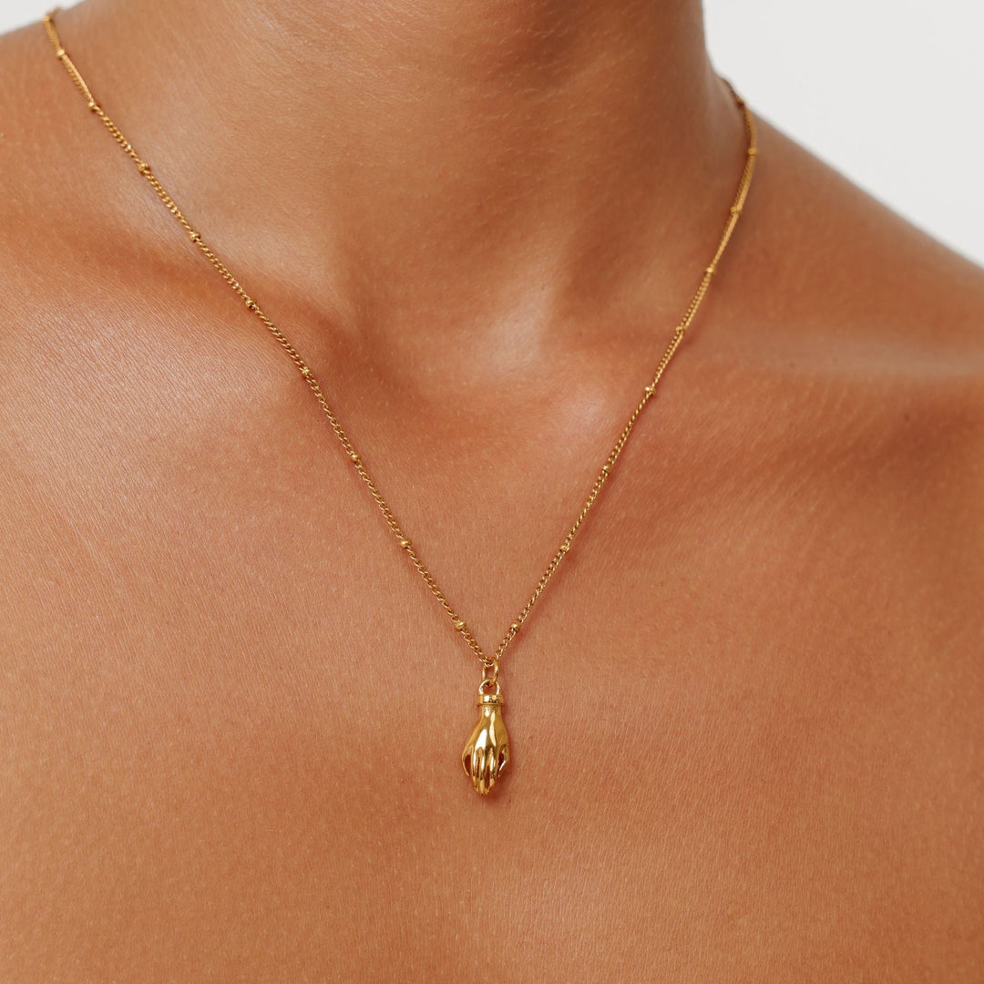 Detailaufnahme der goldfarbenen Schutz Hand Halskette mit grünem Zirkon; symbolischer Damenschmuck.