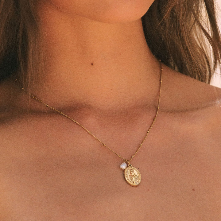 Nahaufnahme der goldenen Kreuz Halskette mit glänzender Süßwasserperle auf zarter Kette.