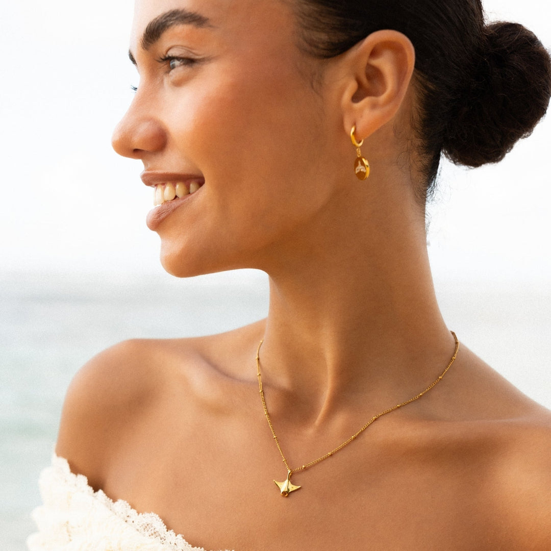 Detailaufnahme: Gold Huggie Creolen für Damen mit glänzendem Zirkon & feiner Walflosse. Wasserfeste Edelstahl Ohrringe, maritim.