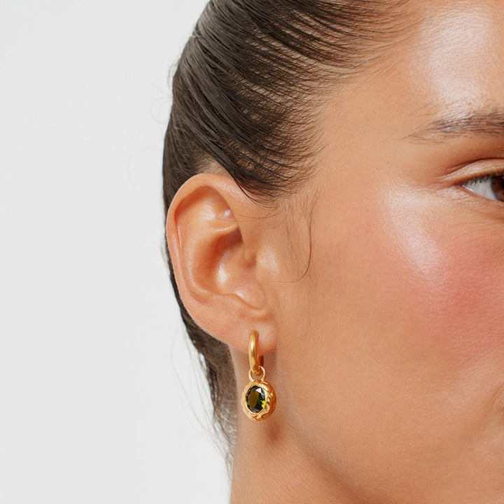 Nahaufnahme: Goldene Creolen für Damen, verziert mit einem leuchtenden grünen Zirkon-Stein.