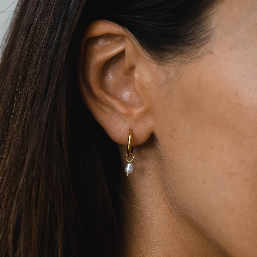 Silberne Damen Huggie Ohrringe mit glänzenden Süßwasserperlen. Moderner wasserfester Schmuck.
