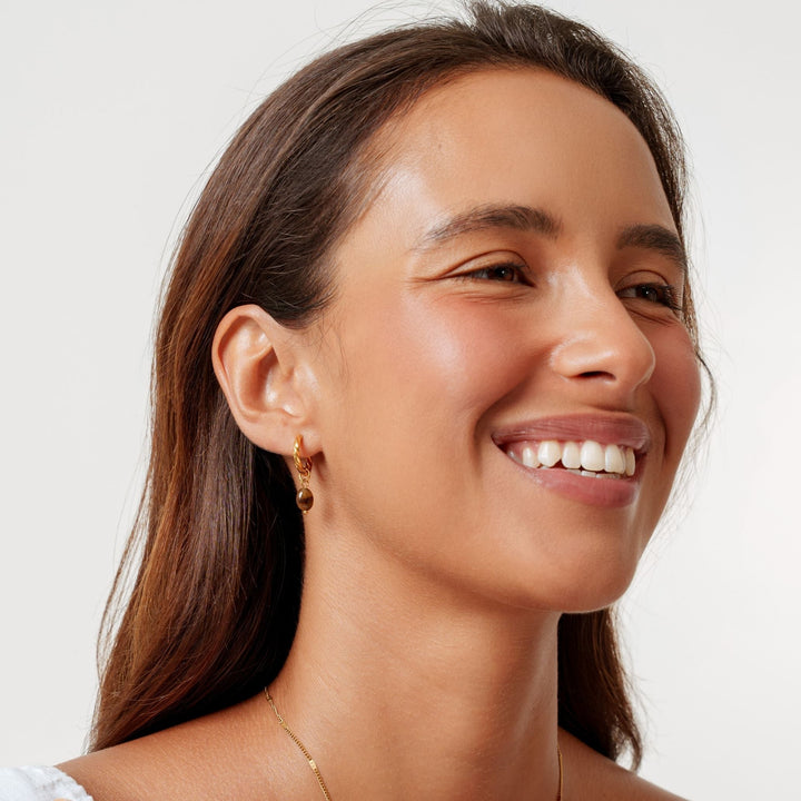 Stylische goldene Damen Huggie Creolen mit Tigerauge Anhänger. Perfekter Schmuck für Alltag & elegante Outfits.