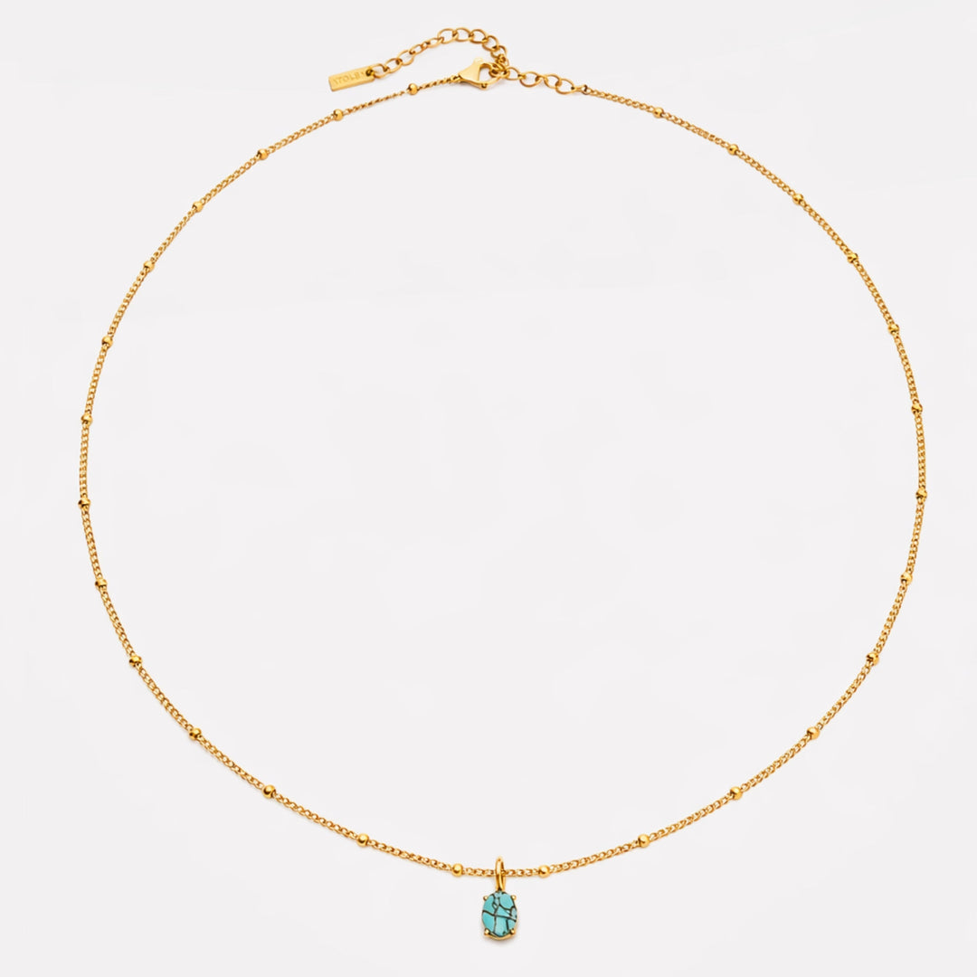 Nahaufnahme der goldenen Damenkette mit glänzendem Türkis-Anhänger und Perlen, hochwertiger Edelstahlschmuck.